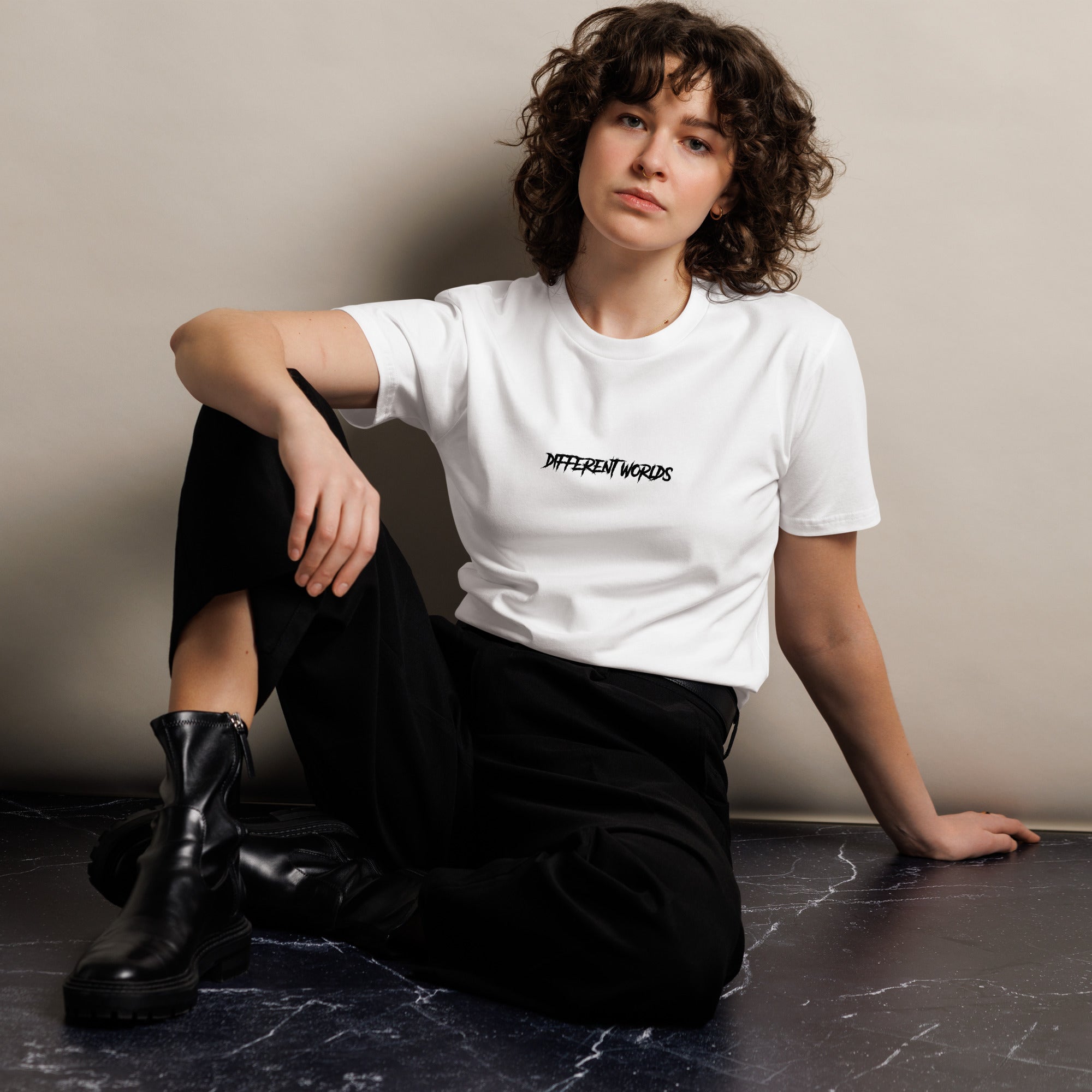 Woman wearing a white t-shirt with text "DIFFERENT WORLDS", sitting on a dark surface against a plain background