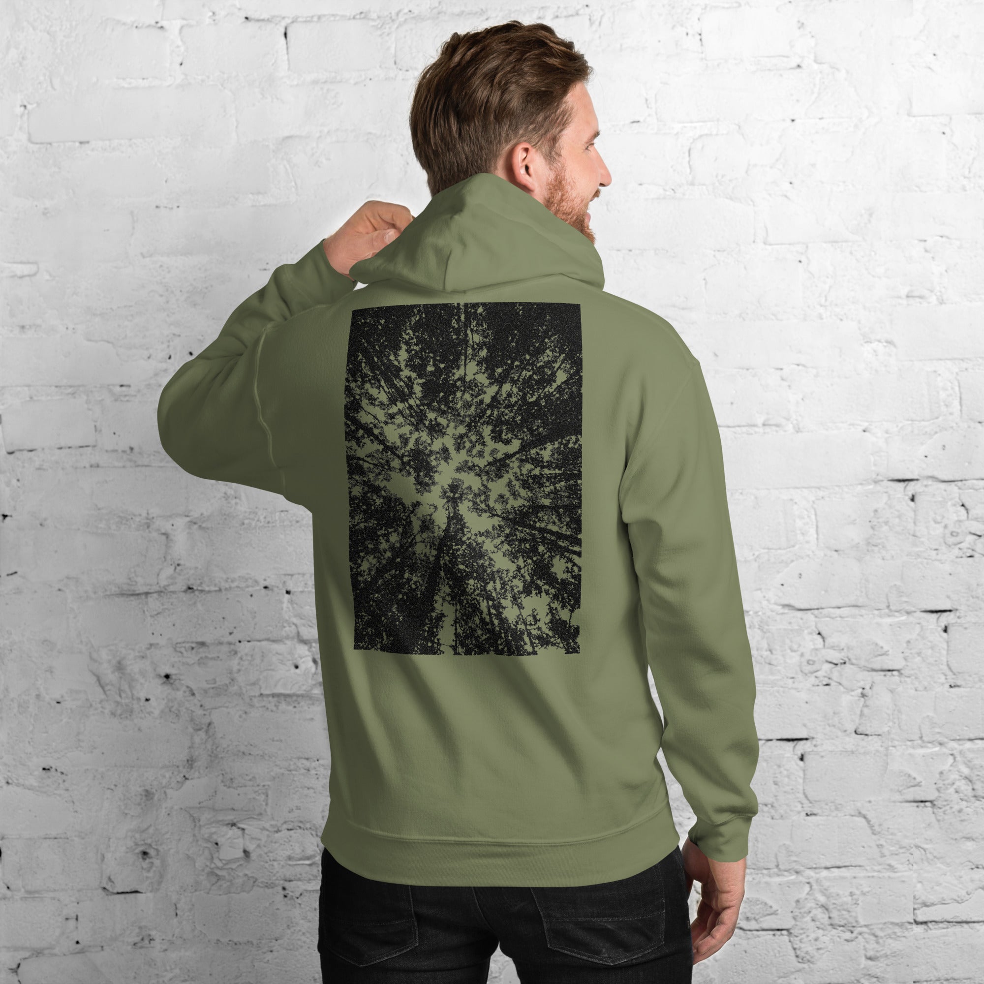 A person wearing a military green hoodie with a black graphic forest print on the back.