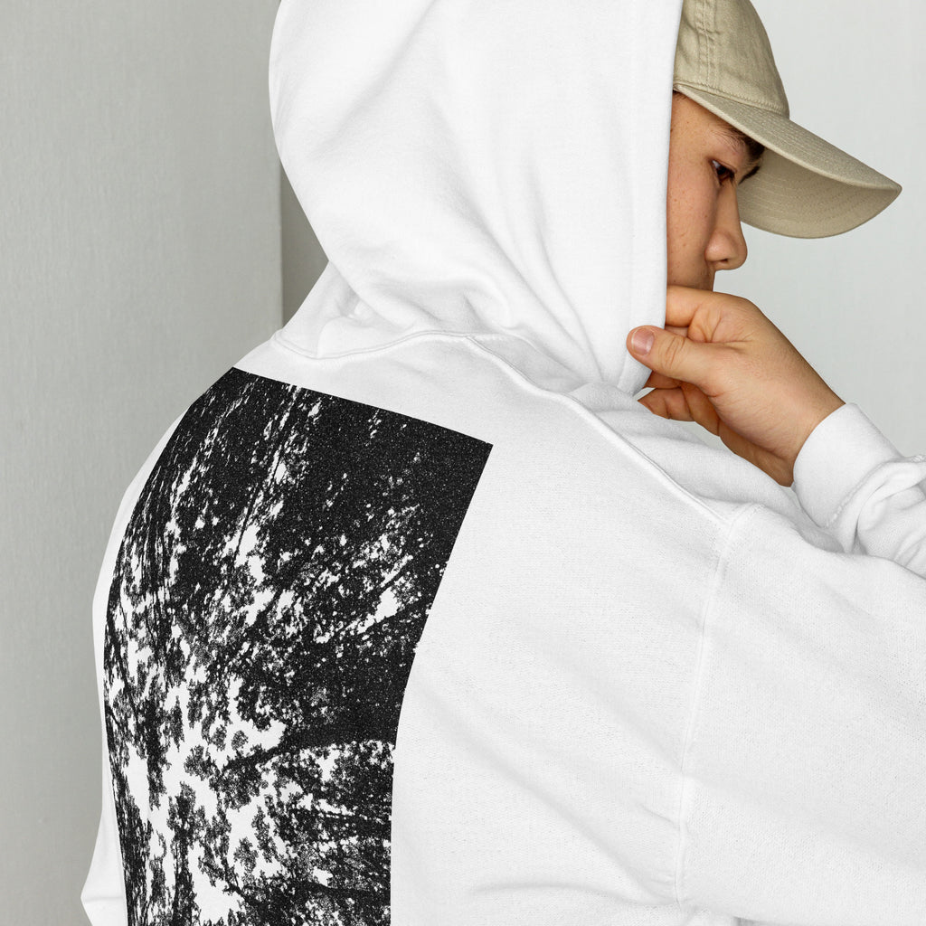 A person wearing a white hoodie with a black forest graphic print on the back.