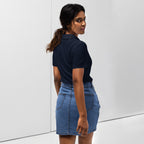 Woman wearing a navy polo shirt with a red love smiley embroidery and a blue denim skirt on a white background. Photography taken from back.
