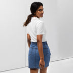Woman wearing a white pique polo shirt with a red love smiley embroidery and a blue denim skirt on a white background. Photo taken from the backside.
