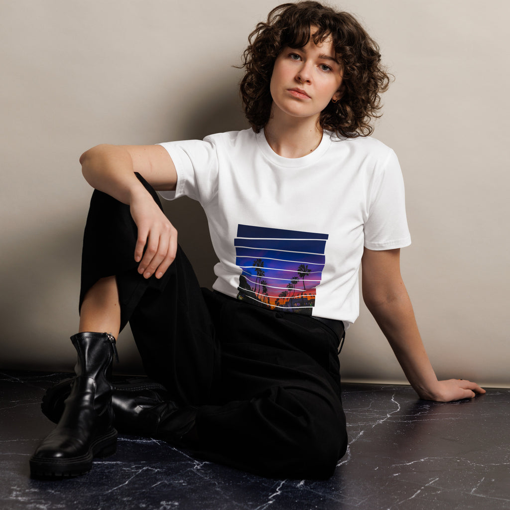 Woman wearing a white sunset t-shirt with a graphic design, sitting on a dark surface against a plain background